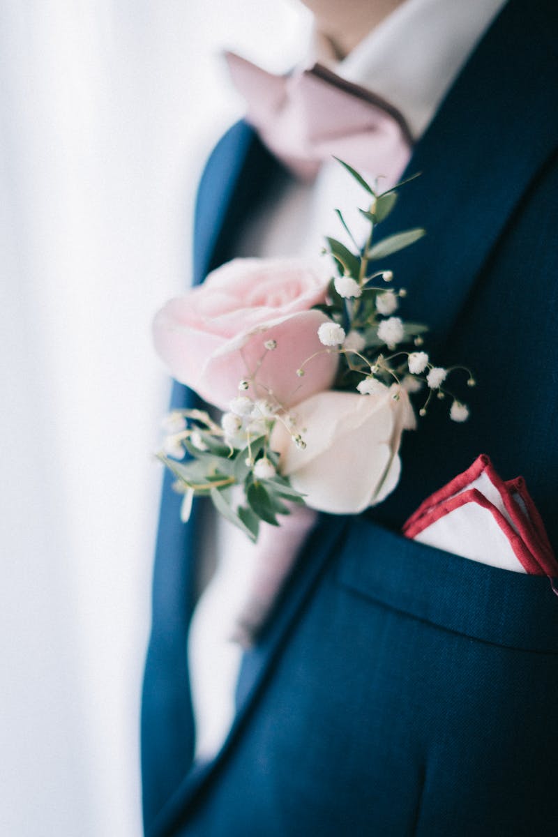 A groom adorns a navy suit with a pink and white rose boutonniere, exuding elegance.